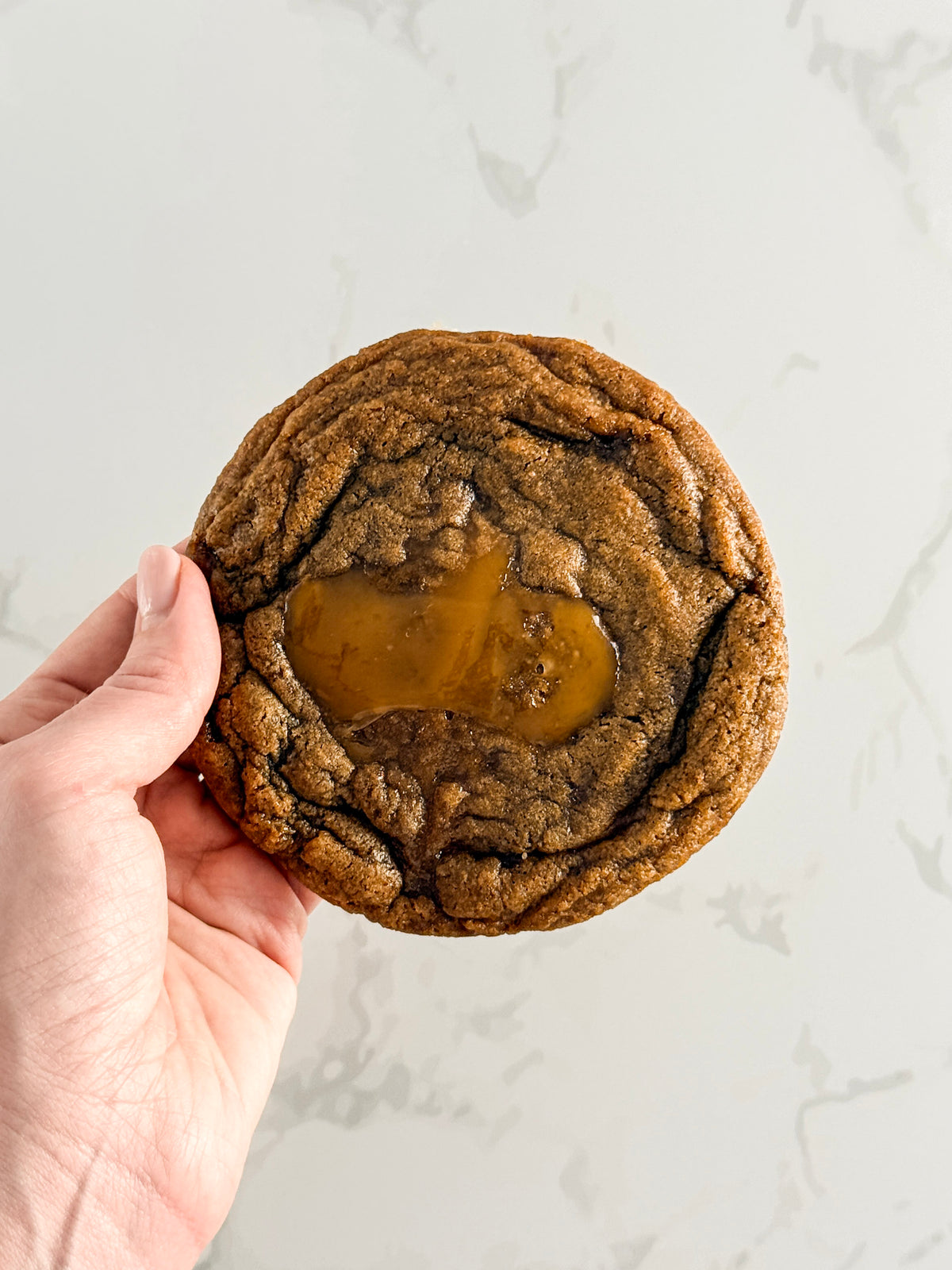 Hand holding a Half Three espresso toffee cookie, showing its size
