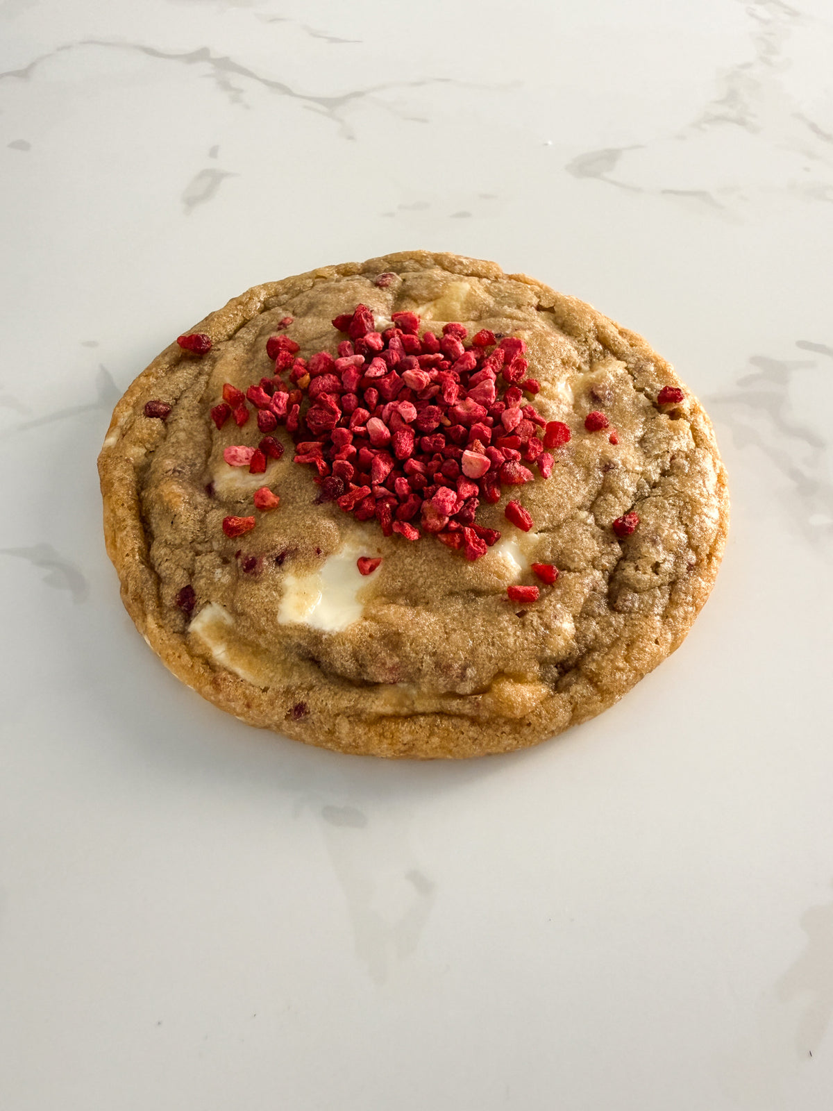 Half Three white chocolate and raspberry cookie from above at an angle, showing pink raspberry pieces and chewy texture