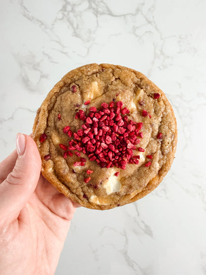 Hand holding a Half Three white chocolate and raspberry cookie with visible freeze-dried raspberries